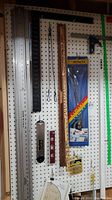 Full pegboard view showing assorted measuring tools including rulers, spirit levels, squares, a boxed protractor, wire twist ties and packaging material.