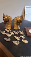 Pair of brass horse head bookends with eleven pewter duck figurines arranged on a table