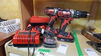 Overview of two red and black Milwaukee M18 cordless drills, multiple chargers, one loose battery pack