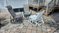 Overview of three outdoor rocking chairs in different colors and a round metal frame glass top table on patio pavers.