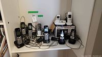 Shelf showing multiple cordless phones from Panasonic and Gigaset, some with cords and charging bases.