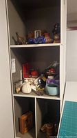 Shelving unit with various sewing related items and decorative keepsakes including figurines, pin cushions, and small framed art.