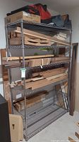 Full view of metal wire storage shelf with multiple wood pieces and storage items on shelves.