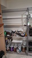 Metal wire storage shelving unit with some stored items including paint cans and tools.