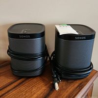 Two stacked Sonos PLAY:1 speakers with power cables wrapped around them on wooden surface