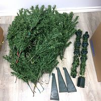 Sections of artificial Christmas tree branches and plastic stand pieces laid out on wood floor.