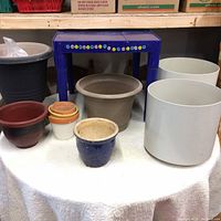 Image showing blue plastic kid's table surrounded by various flower pots placed on a white cloth surface.