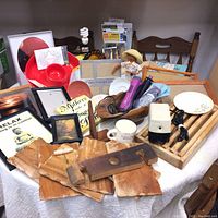 Photo of assorted household collection items on table including wooden slabs, electric pencil sharpener, hair curler, picture frames, vintage maps, mug, small doll, and wooden rack