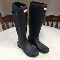 Pair of black knee-high Hunter rubber boots standing upright on a white surface showing left side and front details