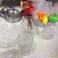 Close-up of metal pet bowls, various glassware including a glass pitcher, popsicle makers with colorful handles, and clear glass serving plates.
