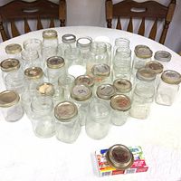 Collection of multiple glass mason jars arranged on a table, some with metal lids, varying in sizes and shapes.