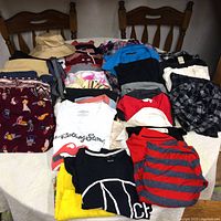 Wide view of all clothing items laid on a table including several shirts, pants, pajama pants, and a beige bucket hat.
