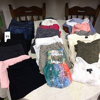Full lot of clothing items laid out on a bed including pants, skirts, blouses, and dresses in various colors and styles.