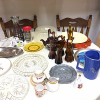 Wide view of all items on table including glass vases, ceramic pitcher, bell, plates, and assorted glassware