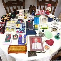 Overview photo of various small household and personal items laid on a table including Pope picture, personal alarm, selfie stick, phone cases, sunglasses, mugs, and decorative pieces.