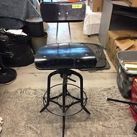 Front view of Toledo swivel adjustable height bar stool showing black metal seat and backrest with wear marks, metal frame with circular footrest, and missing foot pads.