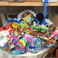 Wide view of the toy collection including inflatable pool, dolls, Woody doll, Chinese checkers game, colorful stacking blocks, and miscellaneous toys.