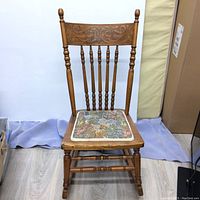 Front view of vintage wooden rocking nursing chair with carved backrest and floral upholstered seat.