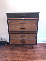 Front view of MCM dresser showing five drawers with black handles, black frame and wood finish drawer fronts.