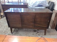 Front view of medium-brown wooden cabinet with sliding door and polished surface.