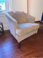 Front-left angled view of cream corduroy chair with dark wooden legs and matching pillow on seat.