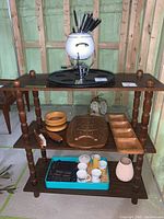 Overall view of shelf with fondue set, wooden trays, ceramic pitcher, and cleaning brushes.