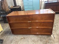 Front view of a wooden 6 drawer dresser with metal handles, placed on a concrete floor.