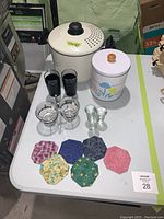 Overview of all items on white table including soup pot, cookie jar, glassware, and fabric coasters
