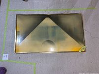 Full view of large hanging wall photo with a geometric abstract design in a brass frame lying flat on the floor.