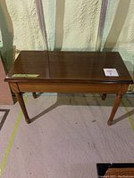 Wooden piano bench showing the full bench from the side front angle, highlighting removable legs and polished wooden surface.