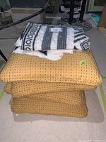 Set of four yellow square pillows stacked with a folded black and white throw blanket on top.