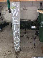 Photo showing the full wooden welcome sign standing next to the metal plant stand in a garage space.
