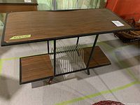 Front and side angled view showing the rectangular table top, metal record rack in center, and two lower shelves with faux wood finish supported by a black metal frame.