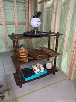 Wooden take apart shelf with various kitchen and decorative items arranged on it in an unfinished room.