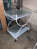 Full side view of the white metal framed tea cart with glass shelves and caster wheels.