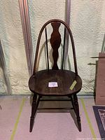 Front view of dark stained wooden chair with rounded seat and curved backrest featuring vertical splat and spindles.