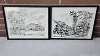 Photo showing both framed Kingston building prints by Trudy Doyle hanging side by side on a brick background