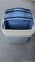 Stack of 7 gray plastic storage tubs with blue-gray lids on top, showing multiple lids stacked inside the tubs.