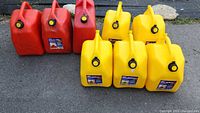 Full shot of 3 red gasoline containers and 5 yellow diesel containers arranged on pavement