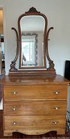 Front view of antique wooden dresser with attached mirror showing full height and decorative mirror frame.