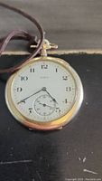 Front view of the Elgin pocket watch, showing white dial with black numerals and hands, and a seconds subdial at 6 o'clock.