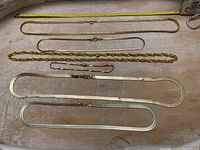 Six gold colored chains and bracelets laid out flat for size comparison with measuring tape.