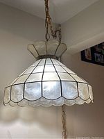 Photo of retro lamp hanging from ceiling showing scalloped stained glass shade with geometric grid pattern and brass-colored chain.