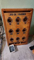 Full view of the vintage wooden bean bag toss game with scoring holes and point values shown, along with container of bean bags at base.