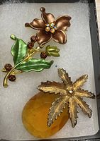 Photo showing both vintage brooches displayed on white padding inside a box.