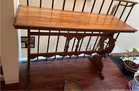 Full side view of wooden sofa table taken near railing, showing wood top and carved side panel with spindle details