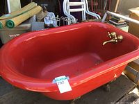 Full view of red claw foot bathtub showing overall form and brass feet.
