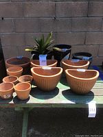 Overview shot showing all clay pots and one potted plant on a green weathered wooden table against a brick wall background.