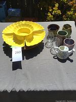 Photo of bright yellow flower-shaped plastic serving tray and handmade earthenware vases with glassware.