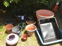 Showcases a variety of pots on grass: several round plastic pots in black, gray, terracotta, green, and ceramic lilac; three rectangular pans stacked on the right.
